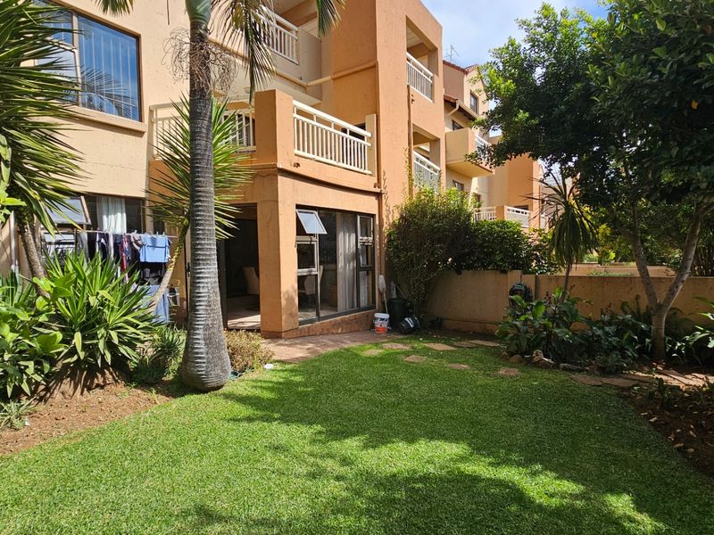 Rear view of the apartment building featuring a private garden, lawn area, and a balcony accessible via sliding glass doors.