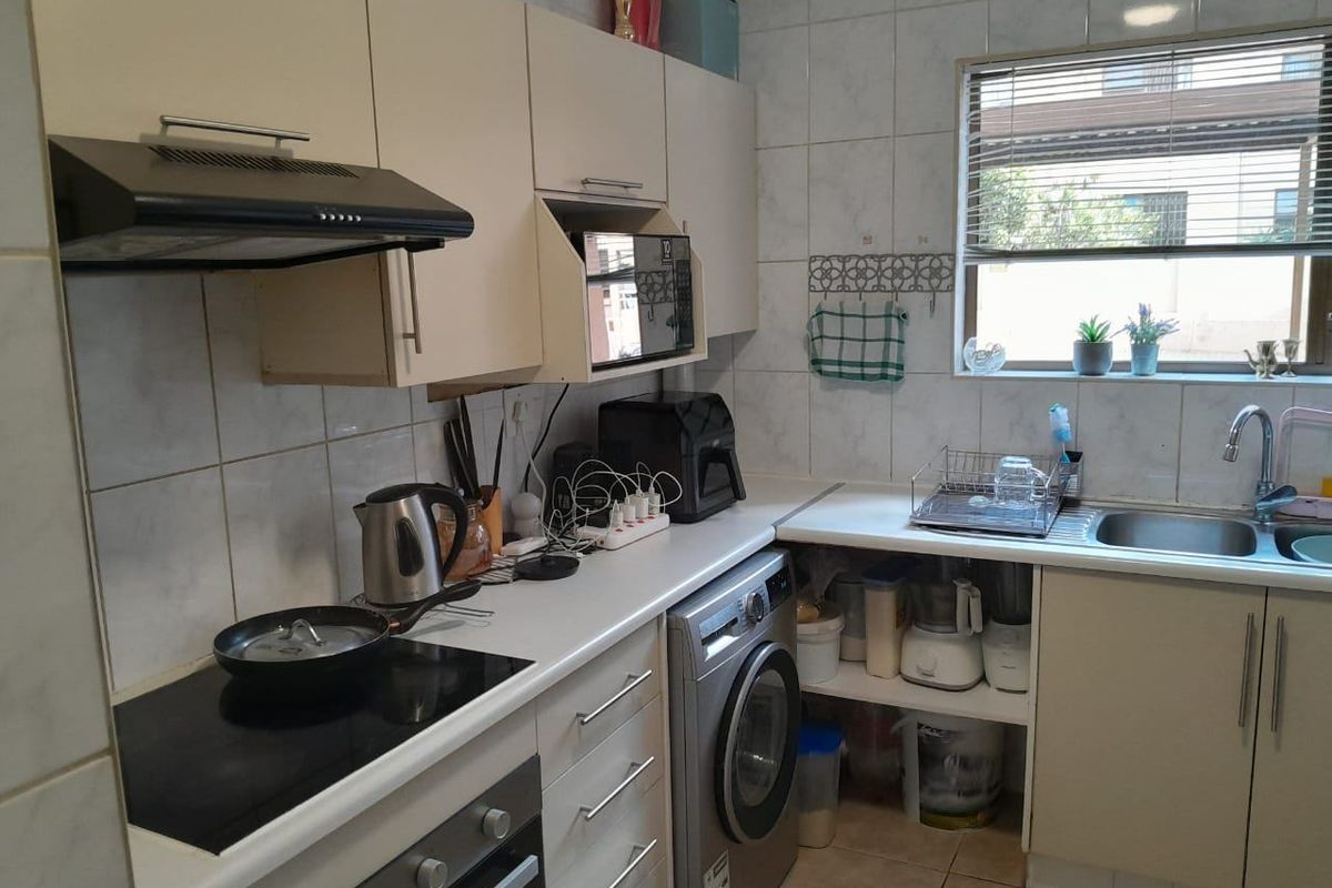 A functional kitchen featuring built-in cabinetry, an electric hob with extractor fan, built-in oven, and a stainless steel sink with tiled backsplash.