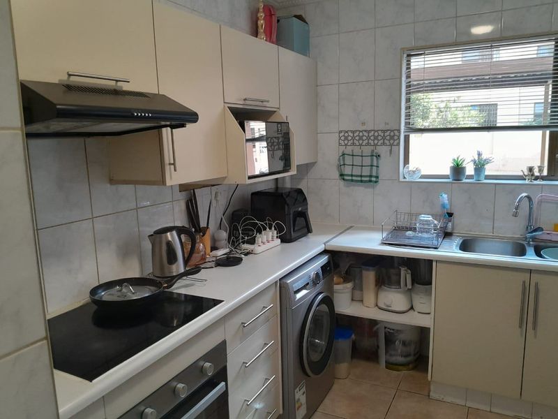 A functional kitchen featuring built-in cabinetry, an electric hob with extractor fan, built-in oven, and a stainless steel sink with tiled backsplash.