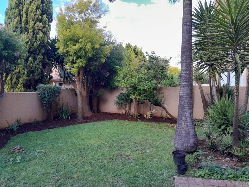 A private garden area featuring a well-maintained lawn, mature trees, and a solid boundary wall for privacy.