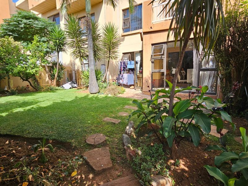 A private rear garden featuring a well-maintained lawn, mature landscaping, and direct access to the apartment through large sliding glass doors.