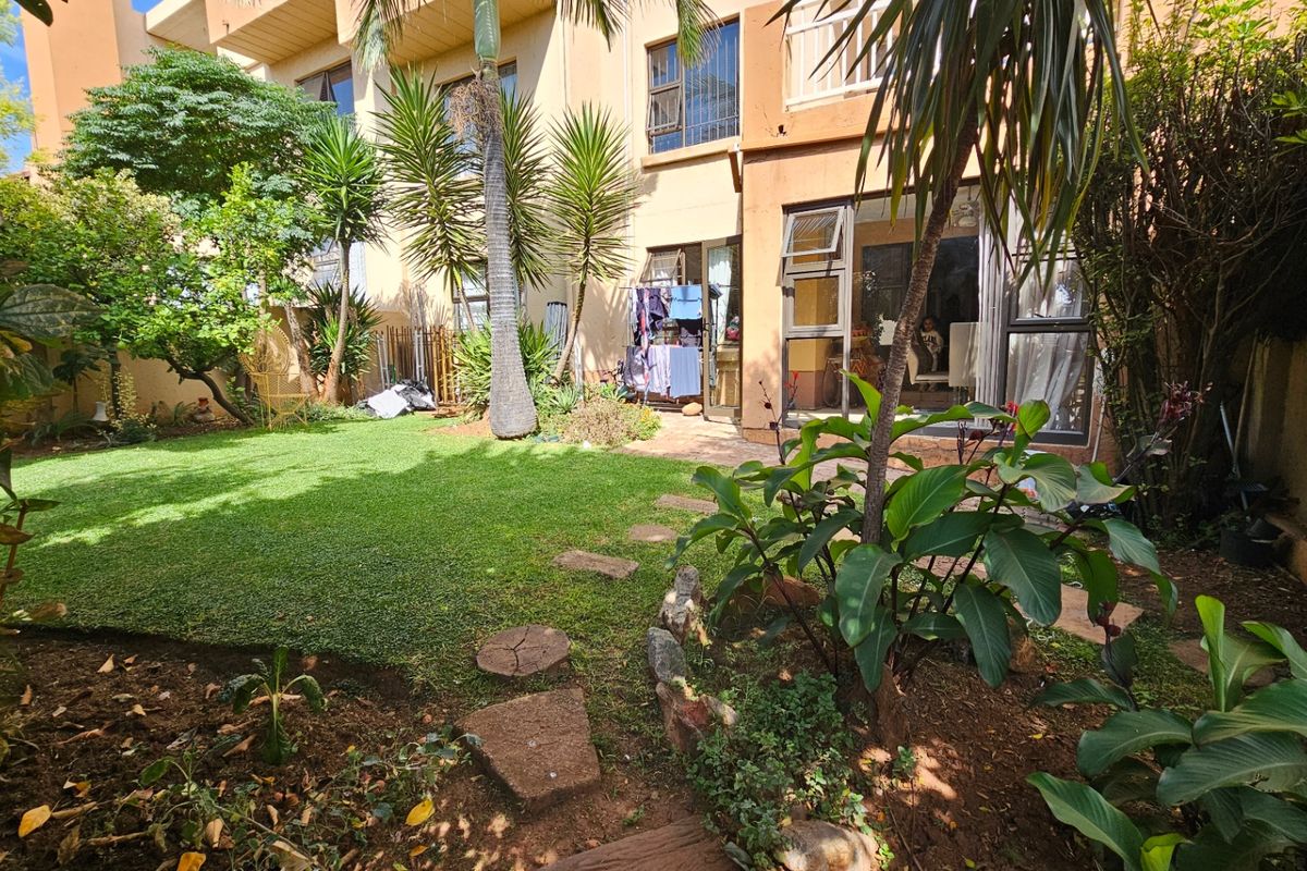 A private rear garden featuring a well-maintained lawn, mature landscaping, and direct access to the apartment through large sliding glass doors.
