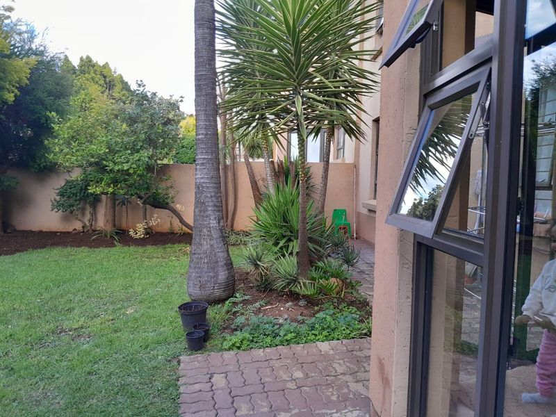 A private rear garden area featuring a paved walkway, established landscaping, and a secure boundary wall, viewed from an adjacent interior space.
