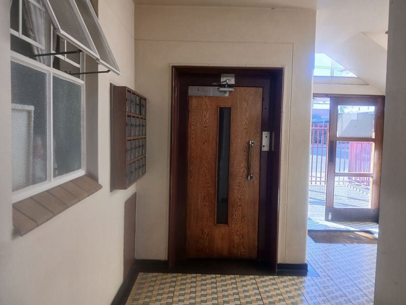 A communal apartment building entrance foyer featuring a secure wooden door, wall-mounted mailboxes, and tiled flooring.
