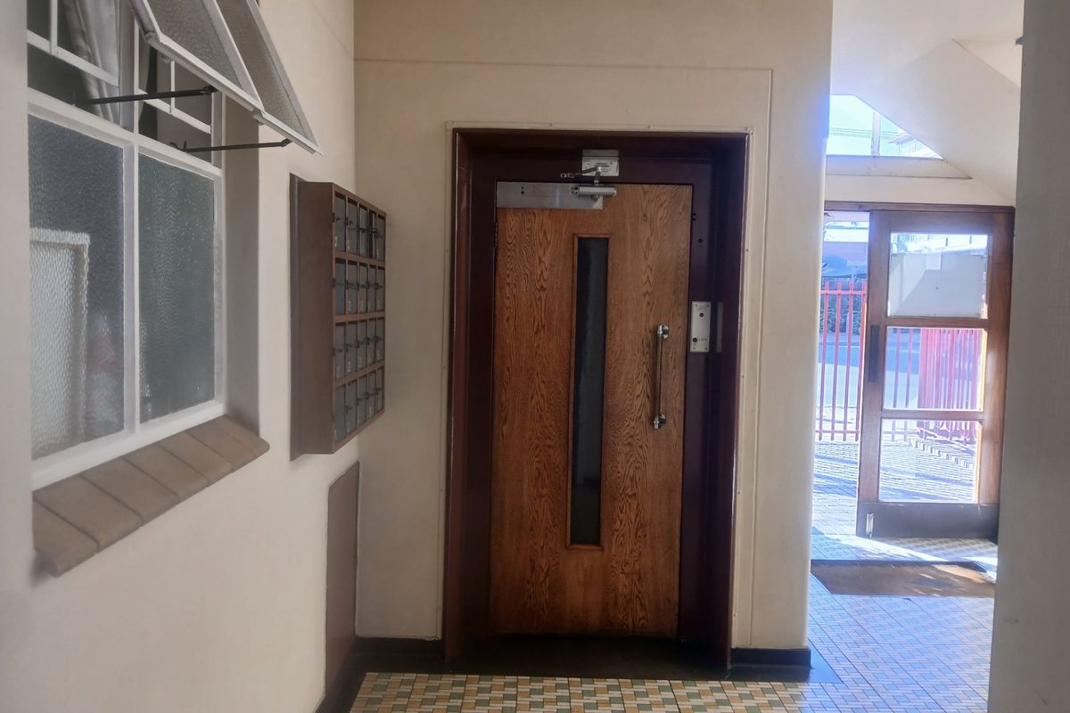 A communal apartment building entrance foyer featuring a secure wooden door, wall-mounted mailboxes, and tiled flooring.