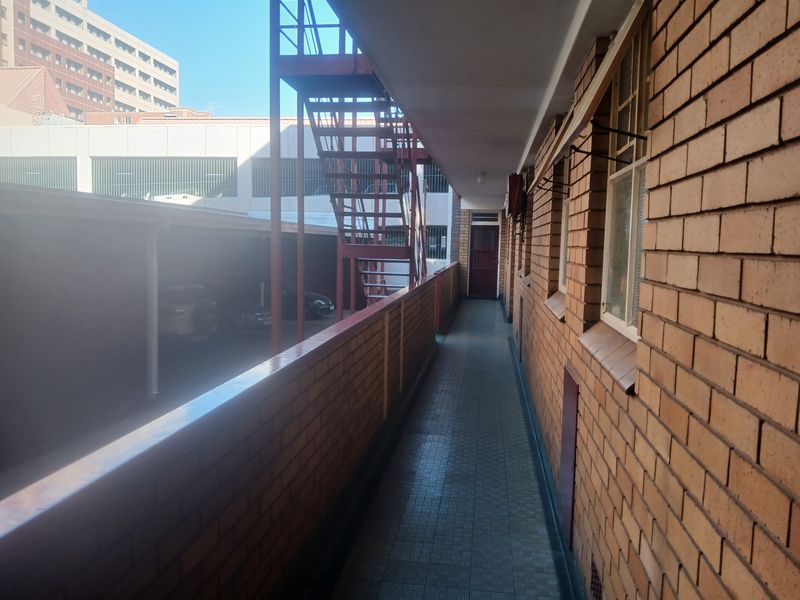 An exterior apartment walkway featuring exposed brick walls, tiled flooring, and a metal fire escape staircase overlooking the parking area.