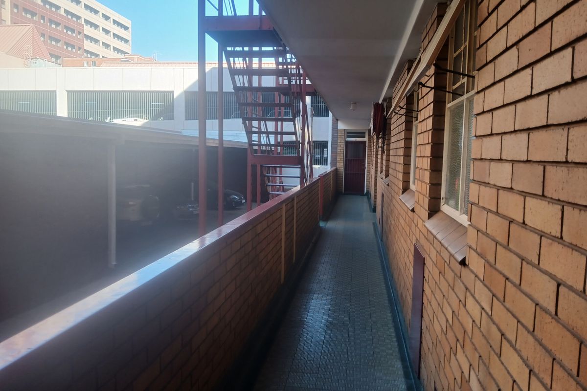 An exterior apartment walkway featuring exposed brick walls, tiled flooring, and a metal fire escape staircase overlooking the parking area.