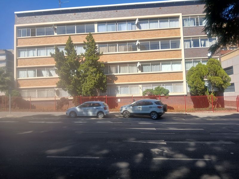 Street-facing view of a multi-story apartment building featuring brick facade, large windows, and secure perimeter fencing.