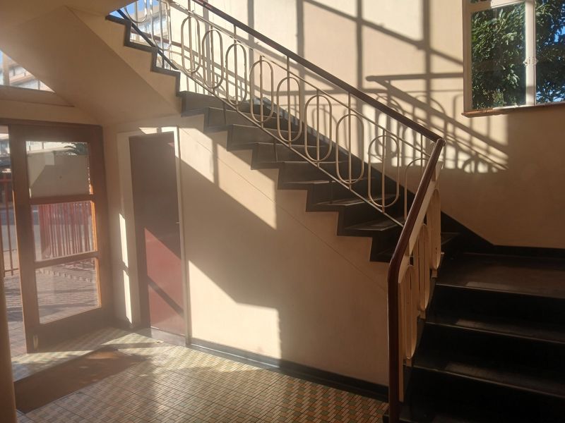 A communal apartment building entrance featuring a staircase with decorative metal railings and tiled flooring, illuminated by natural light from a large window.