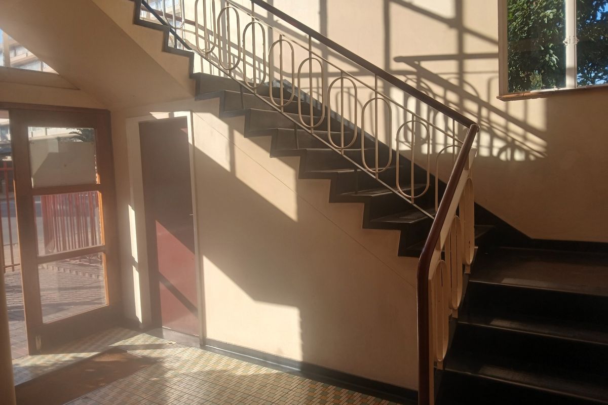 A communal apartment building entrance featuring a staircase with decorative metal railings and tiled flooring, illuminated by natural light from a large window.