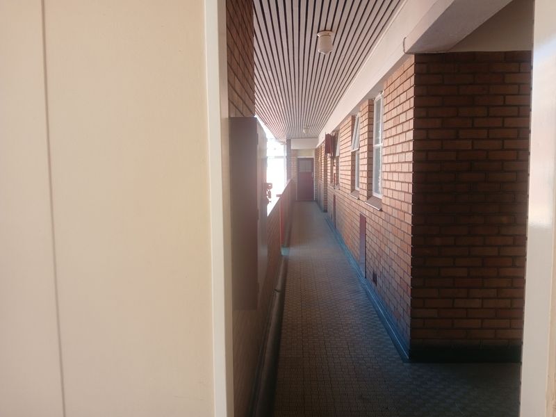 An exterior apartment building corridor featuring exposed brick walls, tiled flooring, and a slatted ceiling design.