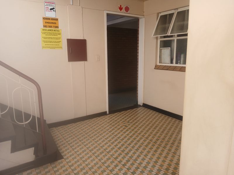 A functional apartment building hallway featuring tiled flooring, a metal staircase railing, and a window providing natural light to the common area.
