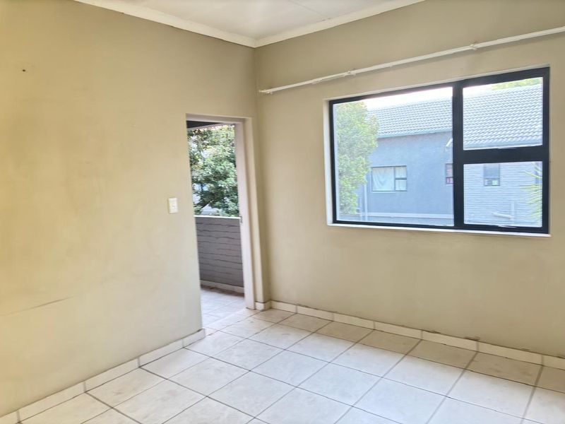 An empty bedroom featuring tiled flooring, neutral walls, and an aluminium-framed window with access to an outdoor balcony area.