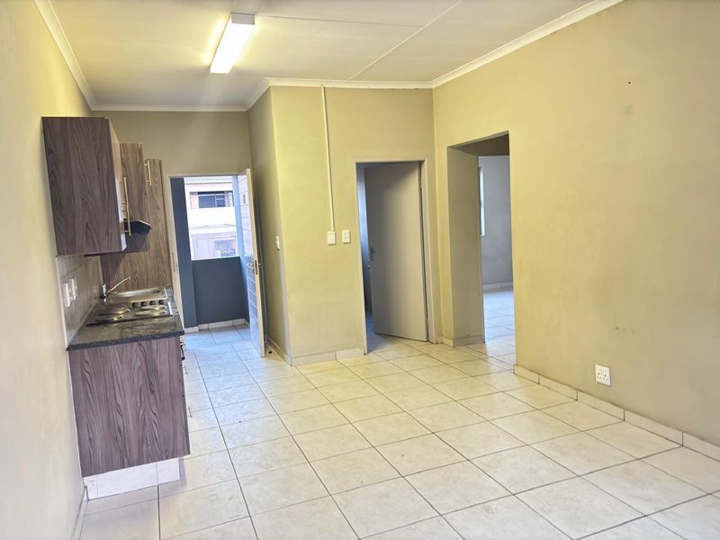A functional kitchen area featuring built-in cabinetry, laminate countertops, and an electric hob, with tiled flooring and direct access to adjacent rooms.