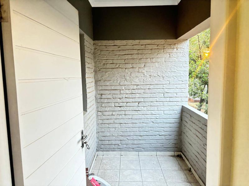 A compact, covered balcony featuring tiled flooring and a painted brick wall, offering a functional outdoor space.