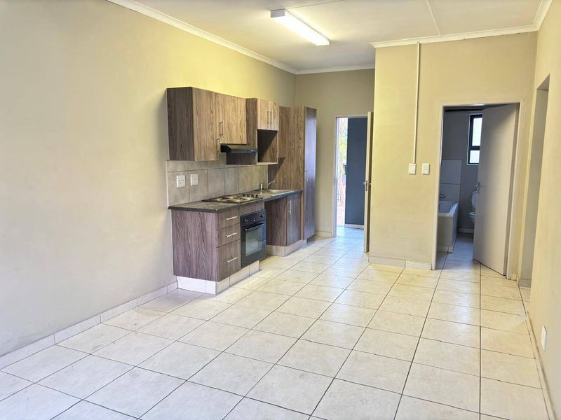Open-plan kitchen area featuring wood-look cabinetry, built-in oven and hob, tiled flooring, and direct access to an adjacent bathroom.
