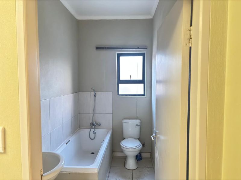 A functional bathroom featuring a bathtub with shower mixer, toilet, and tiled finishes, presenting a clean but dated aesthetic.
