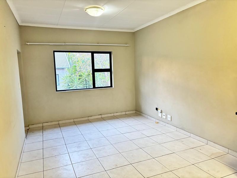 An empty bedroom featuring neutral wall tones, tiled flooring, and an aluminium-framed window, providing a blank canvas for interior design.