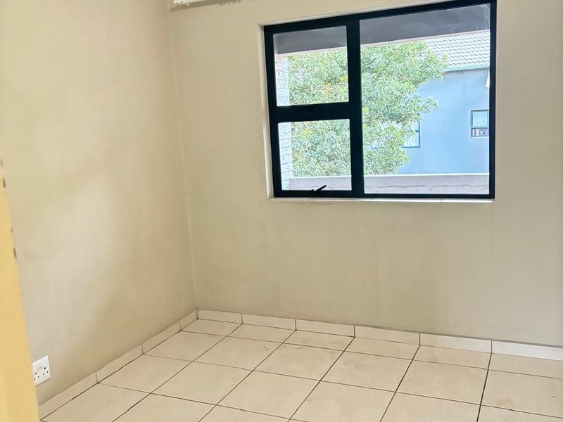 An empty bedroom featuring neutral wall paint, tiled flooring, and an aluminium-framed window with an installed curtain rail.