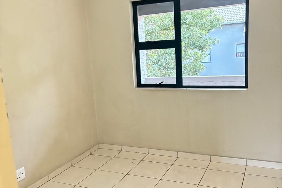 An empty bedroom featuring neutral wall paint, tiled flooring, and an aluminium-framed window with an installed curtain rail.