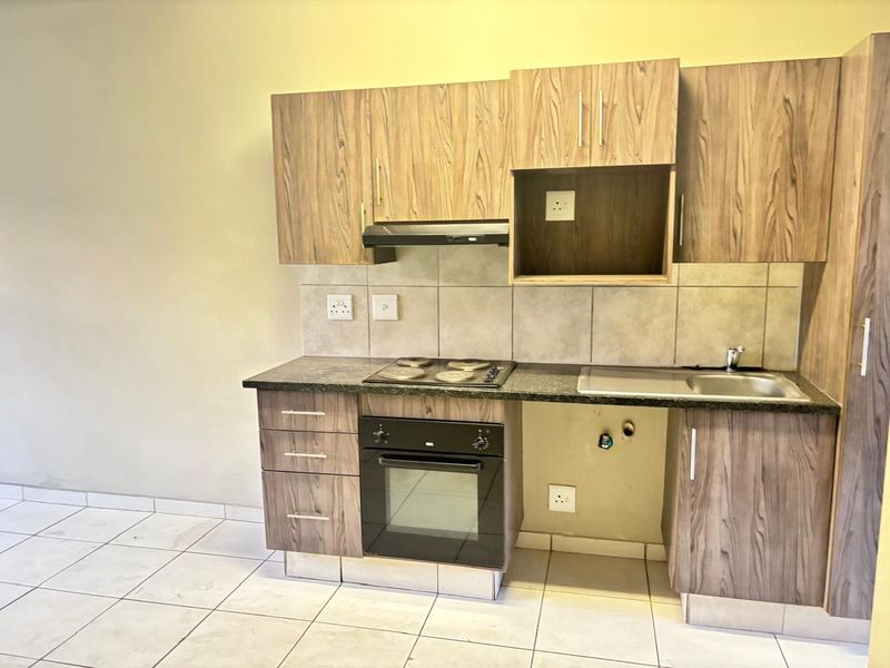 Compact kitchen featuring wood-look laminate cabinetry, granite countertops, built-in oven, electric hob, and tiled backsplash in a clean, functional layout.