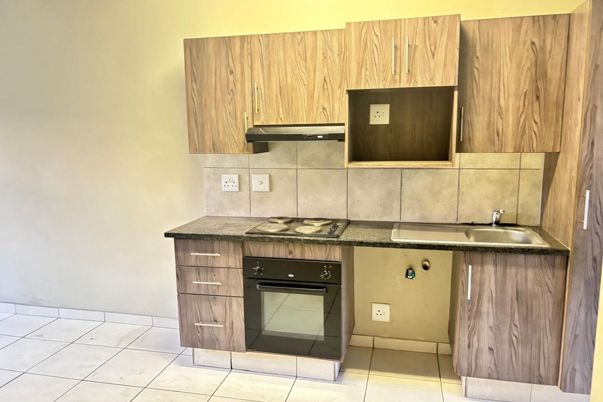 Compact kitchen featuring wood-look laminate cabinetry, granite countertops, built-in oven, electric hob, and tiled backsplash in a clean, functional layout.