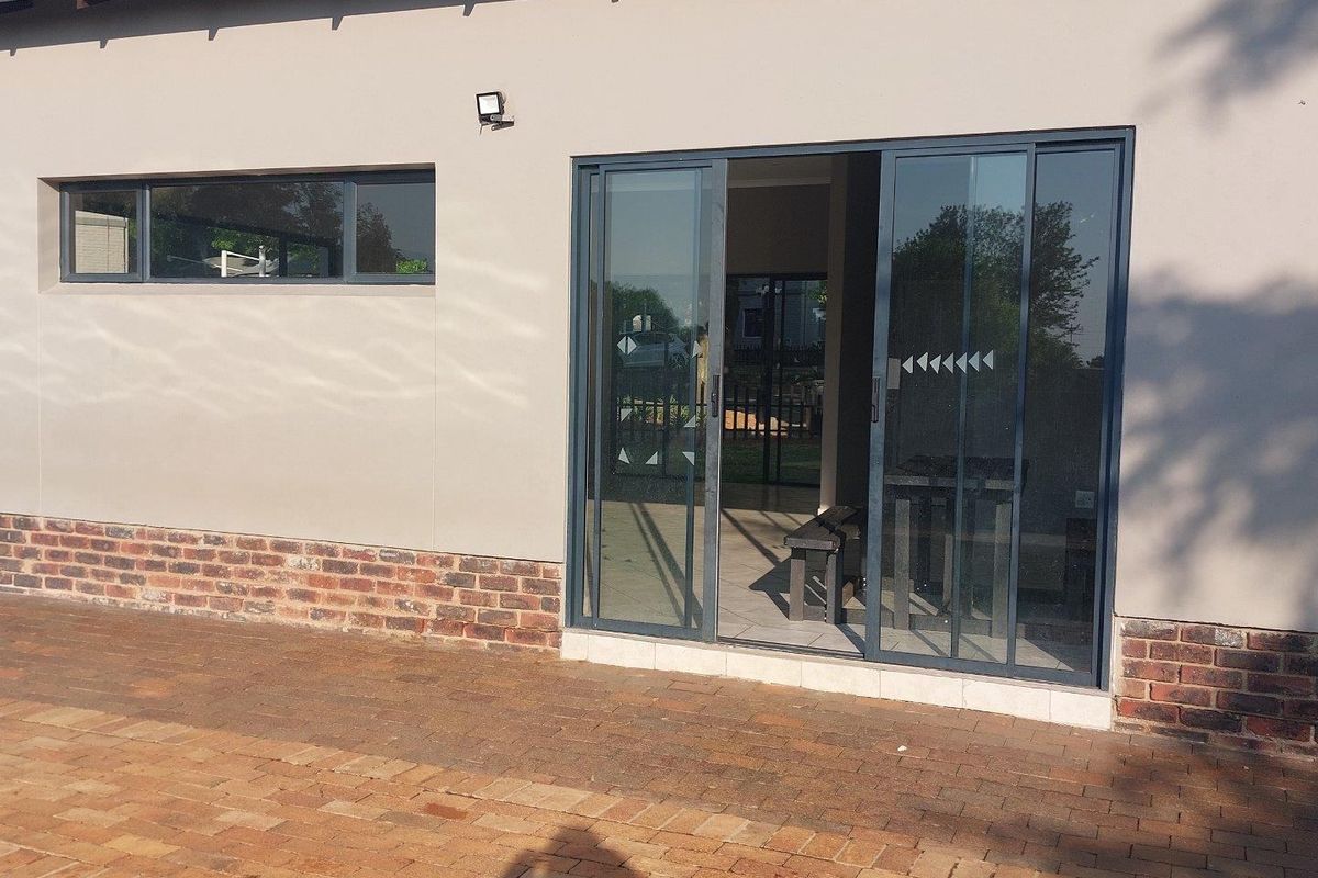 Rear exterior view of the apartment featuring a paved patio, sliding glass doors, and a brick-accented facade.