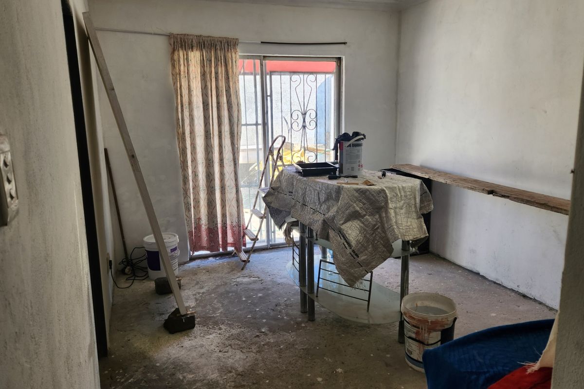 An unfinished living area featuring a sliding glass door with security gate and track lighting, currently undergoing renovation with exposed concrete flooring.