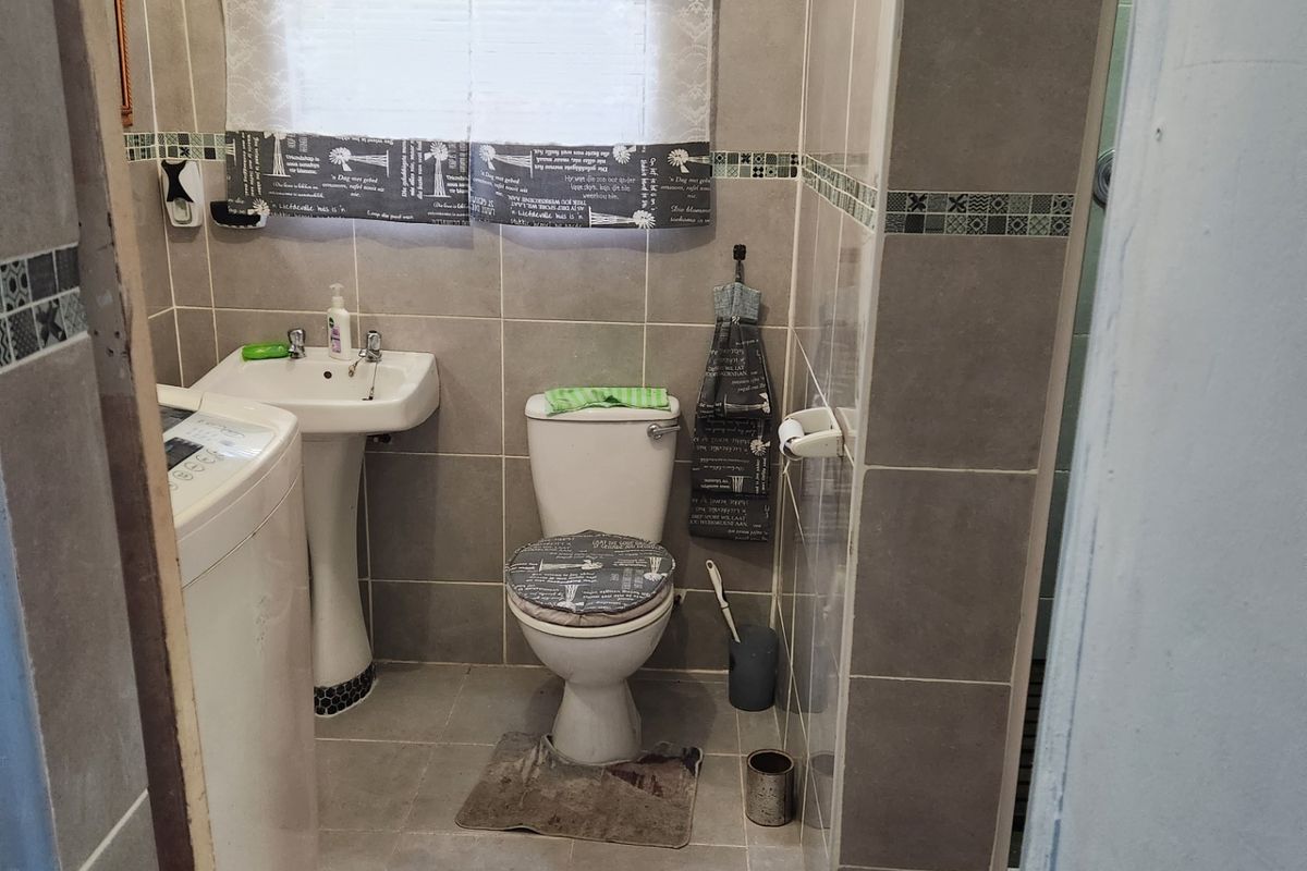 A functional bathroom featuring tiled walls and flooring, a pedestal basin, and a toilet, with an adjacent shower area.