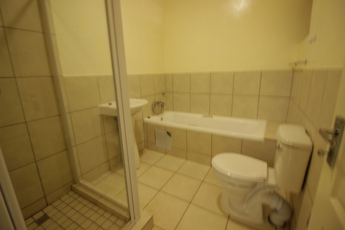 A functional bathroom featuring a bathtub, separate shower enclosure, pedestal basin, and toilet with neutral wall and floor tiling.