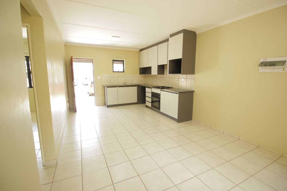 An empty kitchen featuring tiled flooring, built-in cabinetry, a hob, and an oven, with direct access to an exterior doorway.