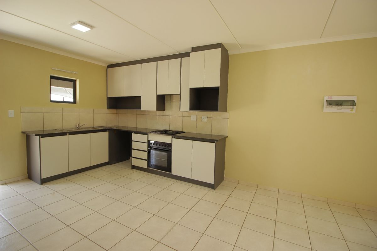 A clean, functional kitchen featuring modern two-tone cabinetry, built-in oven and hob, tiled splashback, and neutral floor tiles in an open-plan layout.