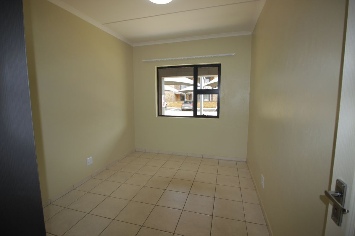 A clean, empty bedroom featuring neutral wall paint, tiled flooring, and an aluminium-framed window providing natural light.