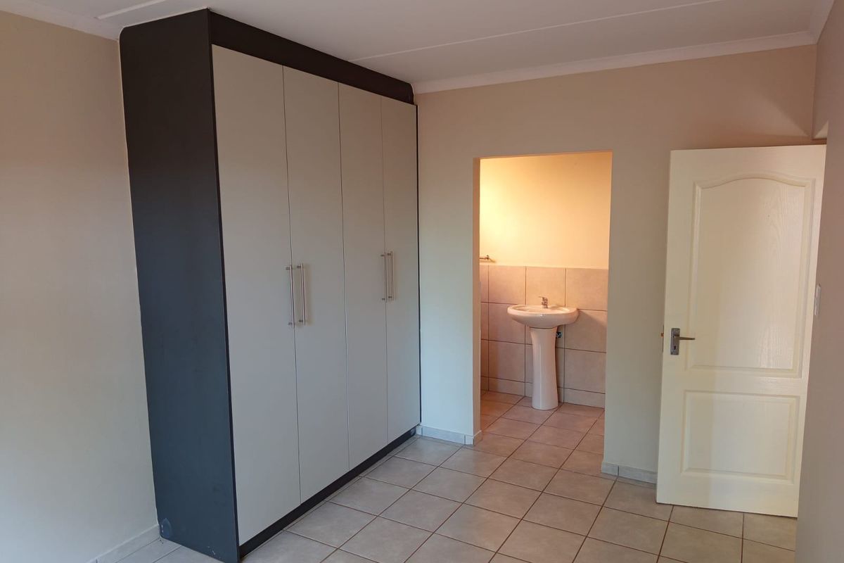 A clean bedroom featuring built-in wardrobes, tiled flooring, and an adjoining en-suite bathroom with a pedestal basin.
