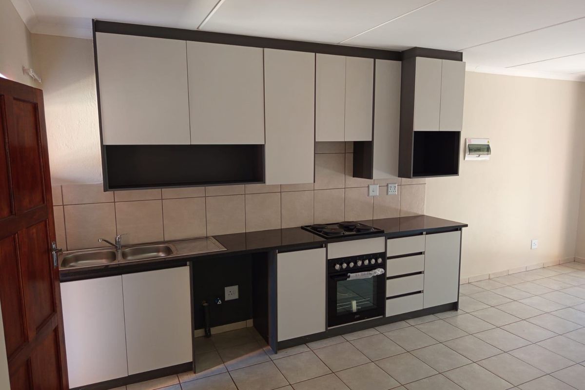 Modern kitchen featuring neutral-toned built-in cabinetry, dark countertops, a built-in oven with hob, and tiled flooring in a clean, well-maintained space.
