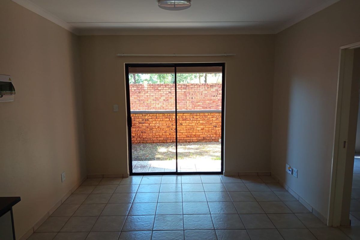 An empty living room featuring neutral walls, ceramic tiled flooring, and a sliding glass door providing access to the rear exterior area.