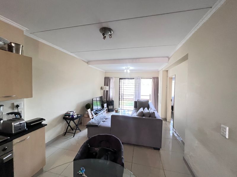 Open-plan living area featuring tiled floors, integrated kitchen cabinetry with built-in oven, and direct access to an outdoor space via a sliding security door.
