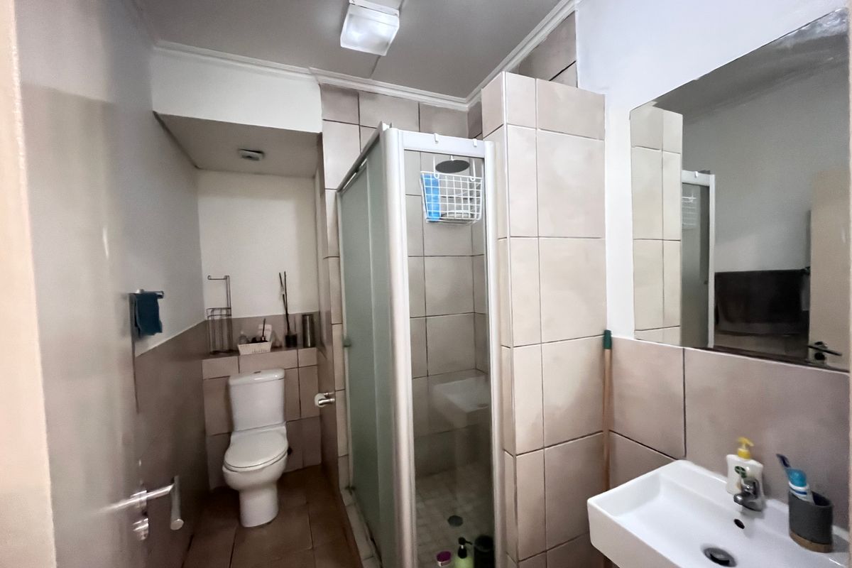 A functional bathroom featuring a shower enclosure, toilet, and wall-mounted basin with tiled finishes throughout.