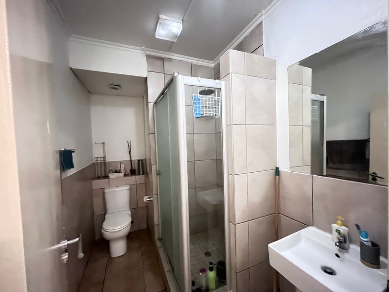 A functional bathroom featuring a shower enclosure, toilet, and wall-mounted basin with tiled finishes throughout.