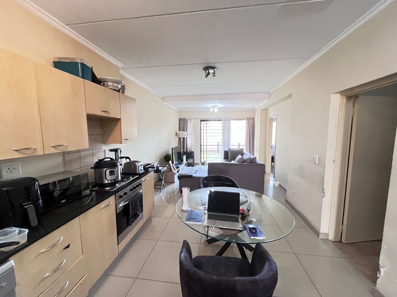 Open-plan living area featuring a functional kitchen with built-in cabinetry, tiled flooring, and direct access to a balcony through a security gate.