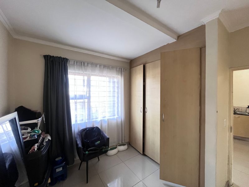 A bedroom featuring built-in wooden cupboards, tiled flooring, and a window fitted with security bars.
