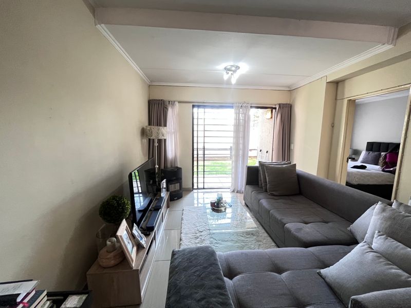 A comfortable living room featuring tiled flooring, ceiling cornices, and a sliding glass door with a security gate leading to an outdoor area.