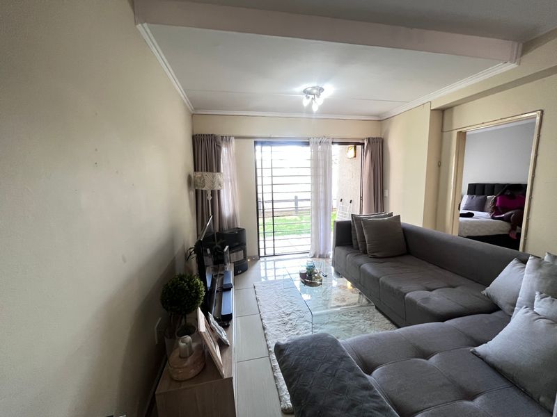 A living room featuring tiled flooring and a sliding glass door with security gate, providing access to an outdoor area.