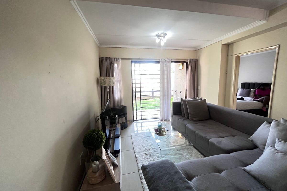 A living room featuring tiled flooring and a sliding glass door with security gate, providing access to an outdoor area.