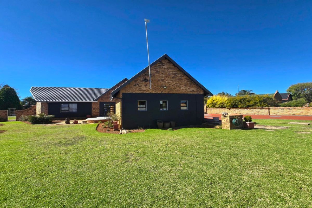 Rear view of the house featuring a brick and painted facade, tiled roof, and a spacious surrounding lawn with boundary wall.