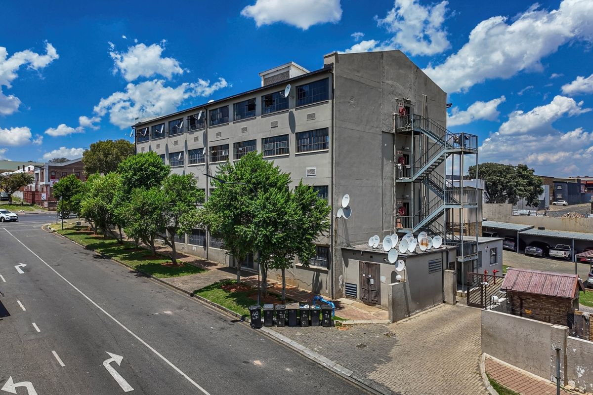 Aerial view of an apartment building exterior featuring a concrete facade, external fire escape staircase, and paved driveway access.
