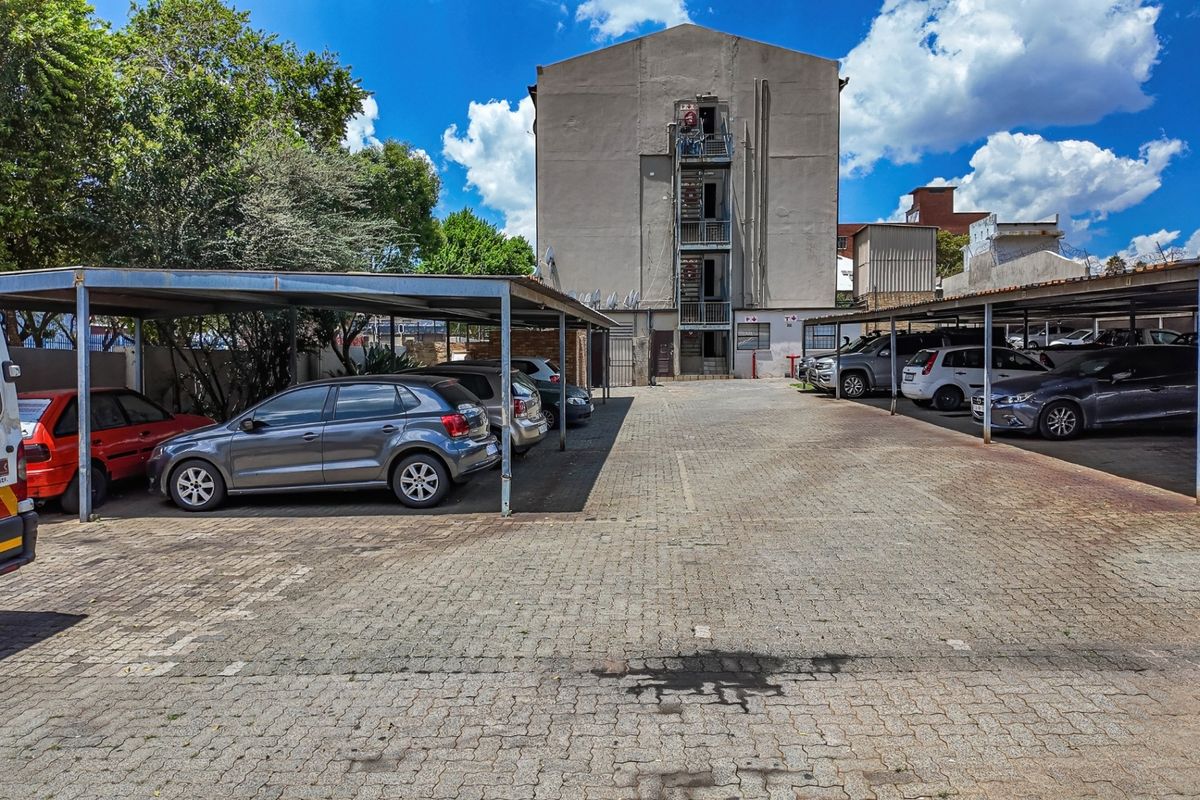 Rear exterior view of the apartment building featuring a paved parking area with covered bays and an external metal fire escape staircase.