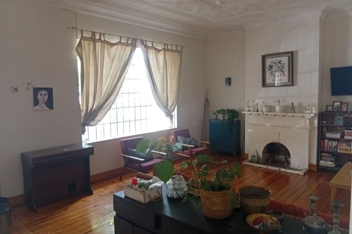 Spacious living room featuring original hardwood flooring, an ornate ceiling, and a traditional fireplace, offering a classic character aesthetic.