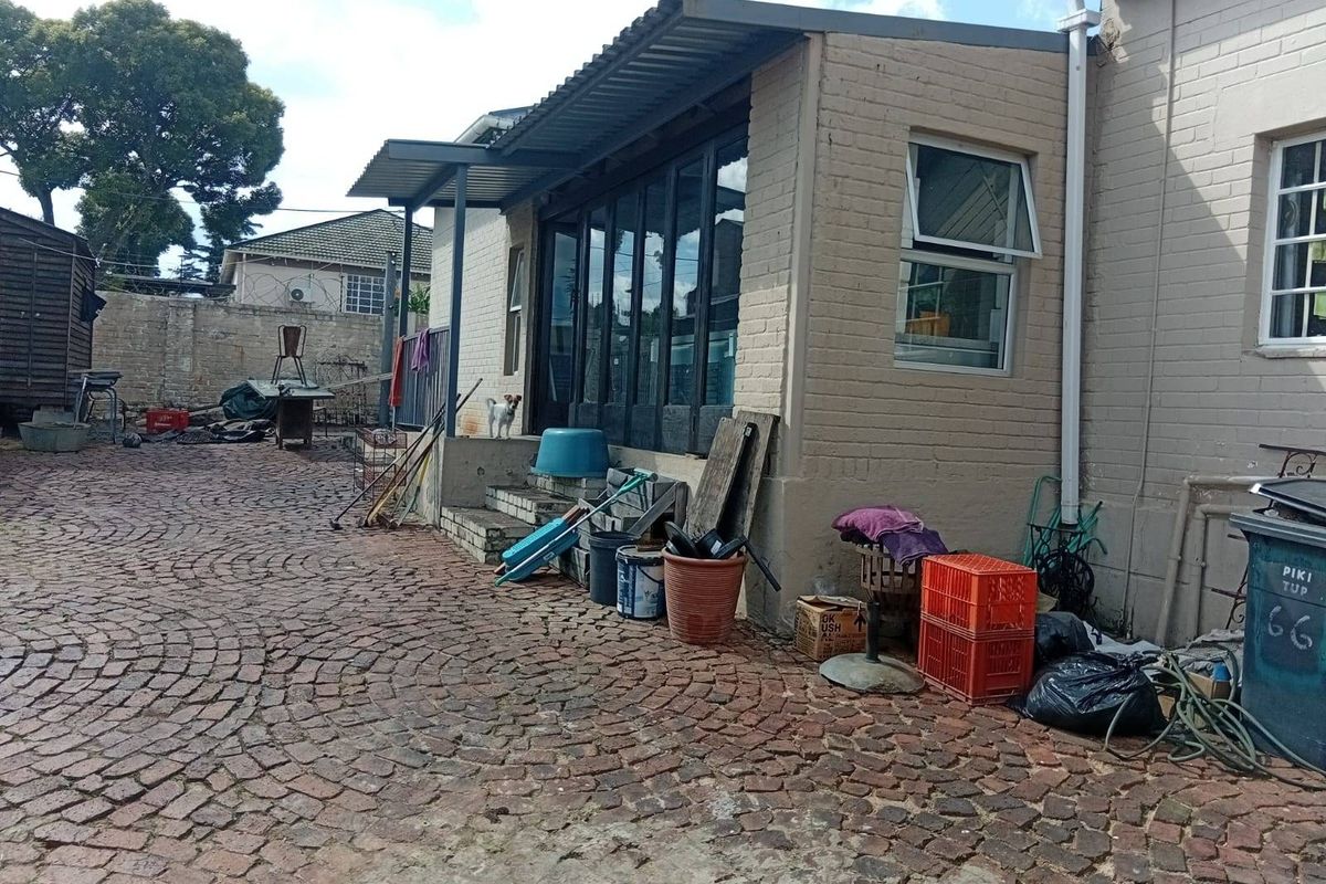 Rear exterior view of the property featuring a cobblestone paved courtyard, brick facade, and a covered patio area with aluminium glass doors.