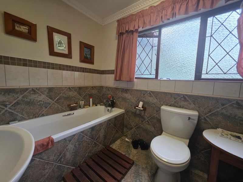 A functional bathroom featuring a built-in bathtub, toilet, and decorative ceramic tiling with leaded glass window detailing.